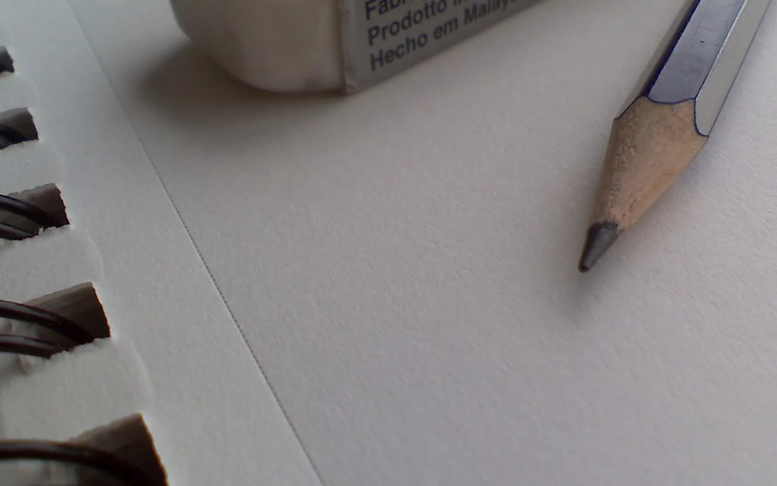 Sharpened graphite pencil and white eraser resting on a blank page of a spiral sketchbook