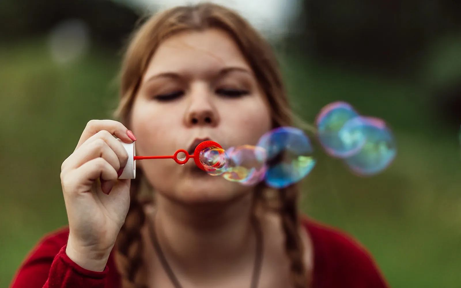 Young woman blowing a stream of iridescent soap bubbles from a red bubble wand outdoors
